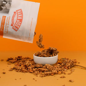 Nana Joes Granola spilling from a bag into a white bowl with an orange background
