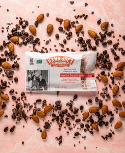 Ocean Beach Granola Bar by Nana Joes Granola on a pink background with almonds and coffee beans