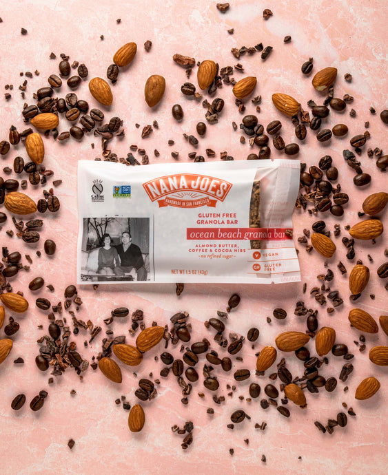 Ocean Beach Granola Bar by Nana Joes Granola on a pink background with almonds and coffee beans