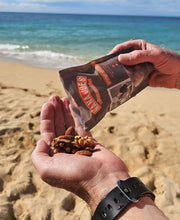 Load image into Gallery viewer, A bag of Orange Spiced Mixed Nuts by Nana Joes Granola being poured into a hand at the beach
