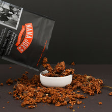 Load image into Gallery viewer, Nana Joes Granola Dark Chocolate blend pouring into a white bowl on a two-tone black background.
