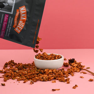 Nana Joes Granola bag spilling into a white bowl on a pink background.