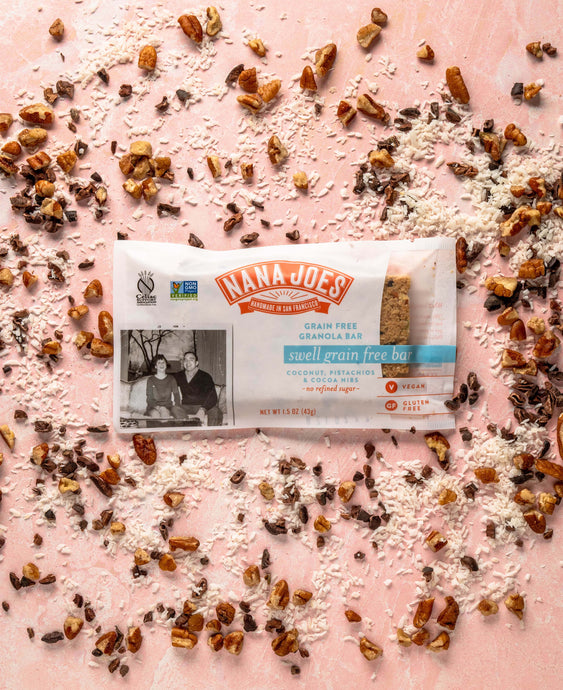 Swell Grain Free Bar by Nana Joes Granola, pink background with coconut and coca nibs sprinkled about