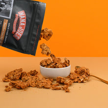 Load image into Gallery viewer, Nana Joes Granola bag spilling into a white bowl on an orange background.
